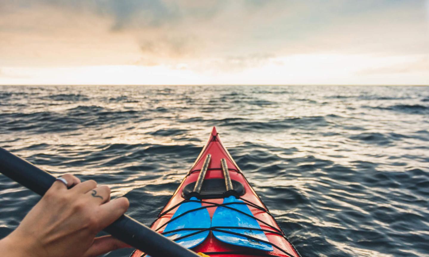 First-person view from a red kayak on the open ocean under a dramatic sunset sky.